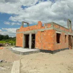 Budowa domu z pustaka żużlowego: dlaczego odchodzi się od tego materiału? Widok na budowę domu z cegły, z widocznymi materiałami budowlanymi.