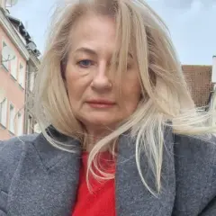 Szafiarka Dorka, ile ma lat? Kobieta w szarym płaszczu i czerwonym swetrze na tle kamienic.