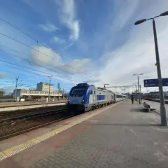 Pociąg na stacji, idealny środek transportu, by dowiedzieć się, jak dostać się do morza. Słońce i chmury na niebie.
