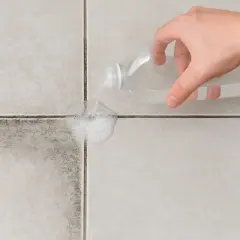 Main d'une personne versant un produit nettoyant sur des joints de carrelage très encrassés pour les faire mousser.