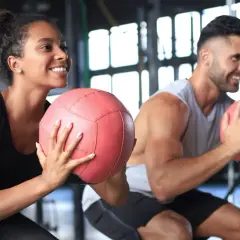 Coppia sorridente si allena in palestra con palle mediche. Non preoccuparti se il primo mese di palestra si ingrassa, è normale!