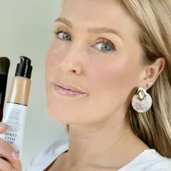 En kvinna håller upp en flaska Giorgio Armani foundation och en borste. Hennes hud ser naturligt fräsch ut.