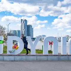 Dzieci bawią się na literach napisu "GDYNIA" na tle miejskiego krajobrazu.