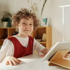 Chłopiec z kręconymi włosami uśmiecha się, trzymając tablet. Czy to wady i zalety szkoły waldorfskiej?