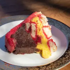 Una fetta di zuppa inglese, con pan di Spagna rosso e giallo e crema al cioccolato, su un piatto decorato.