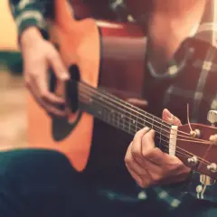 Un uomo con una camicia a quadri suona la chitarra acustica, creando una canzone per salutare colleghi.