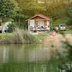 Rodzina odpoczywa nad jeziorem w **camping forteca**. Dzieci pluskają się w wodzie, a dorośli relaksują się na plaży przy domkach.