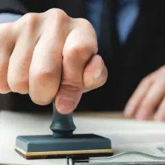 Dłoń z pieczątką nad dokumentem. Zastanawiasz się, czy warto odwoływać się od wyroku sądu? Decyzja wymaga analizy.
