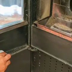 Mano che pulisce il vetro di una stufa a pellet, rimuovendo la cenere per una migliore visione del fuoco.