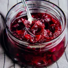 Słoik pełen aromatycznej konfitury z płatków róży, z łyżeczką zanurzoną w rubinowym, gęstym dżemie.