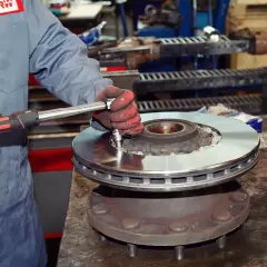 Mechanik w czerwonych rękawicach dokręca śruby podczas wymiany tarcz hamulcowych.