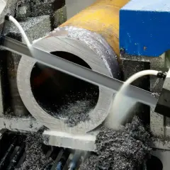 La lame d'une scie à ruban coupe un gros tube métallique, produisant des copeaux.