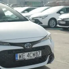 Białe samochody Toyota Corolla, część floty Kinto One, zaparkowane na zewnątrz.