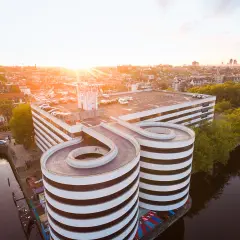 Sonnenuntergang über Amsterdam. Ein Parkhaus mit spiralförmigen Rampen ragt über den Kanal.