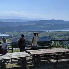 Grupa turystów podziwia rozległą panoramę z widokiem na jezioro i góry. Szlak na górę Wdżar oferuje takie widoki.