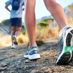 Dwie osoby biegną po kamienistej ścieżce. Zbliżenie na buty biegowe, które są kluczowe, jak przygotować się do biegu na 10 km.