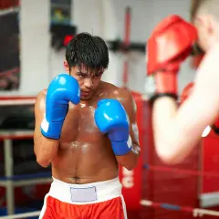 A boxer in blue gloves sweats during a tough boxing cardio workout in the ring, facing an opponent in red gloves.