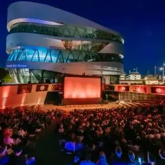 Ein großes Publikum genießt einen Filmabend beim Mercedes-Benz Museum Open Air. Die moderne Architektur des Museums bildet die beeindruckende Kulisse.