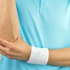 Tenisista z bólem łokcia, być może po teście cozena. Na korcie tenisowym, w niebieskiej koszulce, z opaską na nadgarstku.