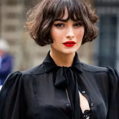 Mujer con un elegante corte de pelo **french bob**, labios rojos vibrantes y una blusa negra transparente con lazada.