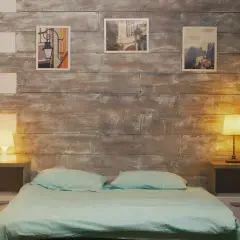 Przytulna sypialnia z drewnianą ścianą, łóżkiem i lampkami nocnymi. Obrazki na ścianie dodają uroku tej ślepej sypialni.