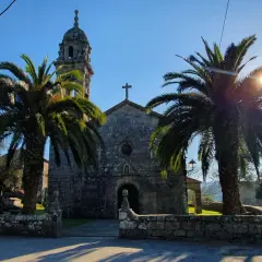 Iglesia de piedra con palmeras y sol brillante. Un lugar tranquilo que ver en Rianxo, ideal para pasear.