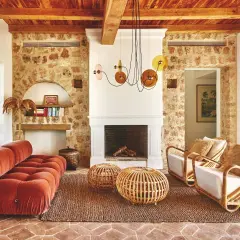 Gemütliches Wohnzimmer im Boho-Stil mit Terrakotta-Boden, Steinwand, Korbmöbeln und einem roten Samtsofa. Die boho bedeutung zeigt sich in der entspannten Atmosphäre.