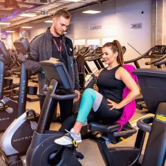 Trener pomaga kobiecie na rowerku stacjonarnym. Czy MCFit honoruje Multisport? Sprawdź, zanim zaczniesz trening!