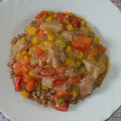 Gulasz wieprzowy z warzywami na kaszy gryczanej. Danie zawiera kawałki wieprzowiny, marchewkę, kukurydzę, groszek i paprykę.