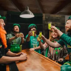 Glada människor med gröna hattar och skägg skålar med gröna drinkar vid en bardisk. Perfekt för roliga teman!