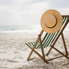 Leżak plażowy z kapeluszem na oparciu, gotowy na wczasy pod gruszą. Piasek, morze i słońce czekają.