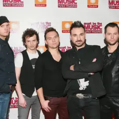 Pięciu mężczyzn w strojach scenicznych pozuje do zdjęcia na tle ścianki z logo "Must Be The Music".