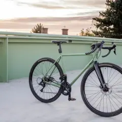 Zielony rower gravel z szerokimi oponami i pedałami platformowymi, idealny do odkrywania różnych rodzajów terenu.
