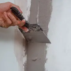 Mano con spatola riempie un buco nel muro con stucco, riparando la parete.