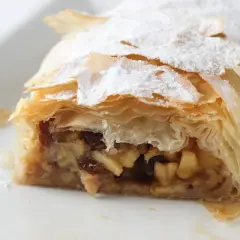 Un trozo de strudel de manzana, con su masa hojaldrada y relleno de manzana y pasas, espolvoreado con azúcar glas.