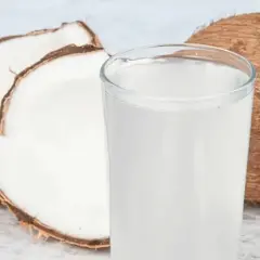 Ein Glas erfrischendes Kokoswasser steht neben einer aufgeschnittenen Kokosnuss. Kokoswasser gesund und lecker!