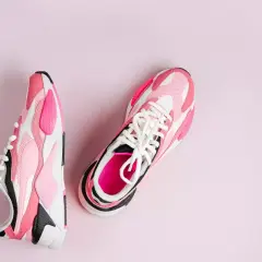Różowe i białe buty sportowe, które wyglądają jak najszybsze buty do biegania, leżą na jasnoróżowym tle.