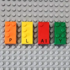 Vier bunte LEGO-Steine bilden das Wort "PLAY". Die Steine sind orange, gelb, rot und grün. Das Erkennen von LEGO-Steinen ist der erste Schritt zum Bauen.