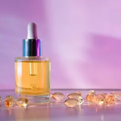 Szklana buteleczka z serum i kapsułki, które mogą zawierać retinol lub retinal, na tle fioletowo-różowego gradientu.