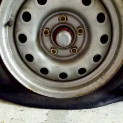 Un clavo en rueda coche ha causado un pinchazo. La llanta metálica y el neumático desinflado se ven sobre el suelo de cemento.