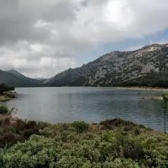 Paisaje sereno de lagos en Mallorca, rodeado de montañas rocosas y vegetación exuberante bajo un cielo nublado.