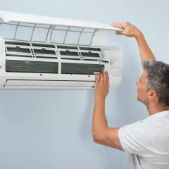 Mężczyzna sprawdza klimatyzację, która raz działa raz nie. Otwiera obudowę, by przyjrzeć się mechanizmowi.