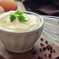 Cremige Mayonnaise ohne Ei, garniert mit Petersilie, neben Eiern und Pfefferkörnern.
