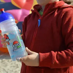 Kind hält eine isybe trinkflasche mit Tauchermotiv. Im Hintergrund bunter Drachen.