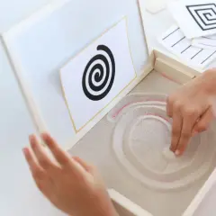 Niño practicando preescritura montessori, trazando espirales en arena.
