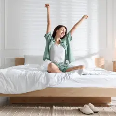 Femme s'étirant sur un lit bas, profitant de la lumière du matin. La faible hauteur du lit crée une ambiance paisible.