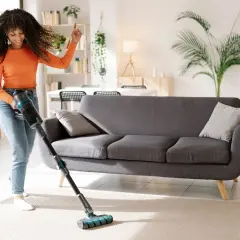Mujer sonriente aspira el suelo con una aspiradora sin bolsa, bailando al ritmo de la limpieza.