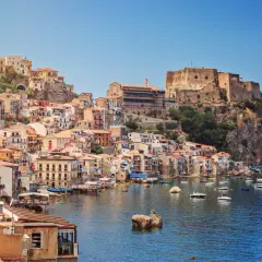 Colorful houses cascade down a cliffside to a harbor filled with boats, overlooking the sea. This is one of the picturesque cities in Calabria, Italy.