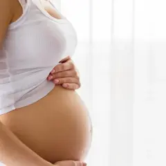 Brzuch kobiety w białej koszulce, trzymający go dłońmi. To piękny widok, który przypomina o cudzie życia i przyszłym teście pappa.