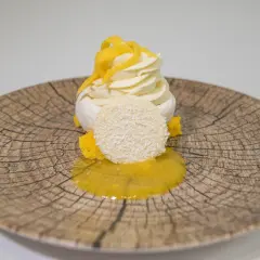 Deliciosa pavlova de mango con merengue, crema batida, coco rallado y salsa de mango sobre un plato rústico.